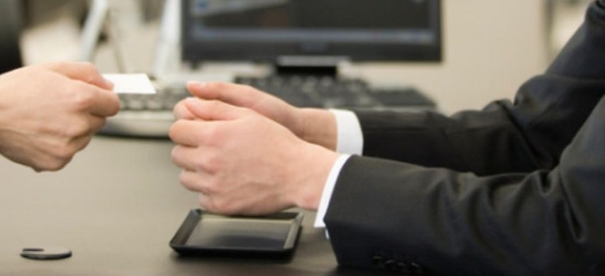 Two professionals exchanging a business card across a desk
