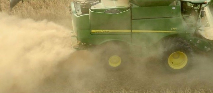 Combine harvesting a grain field in a cloud of dust